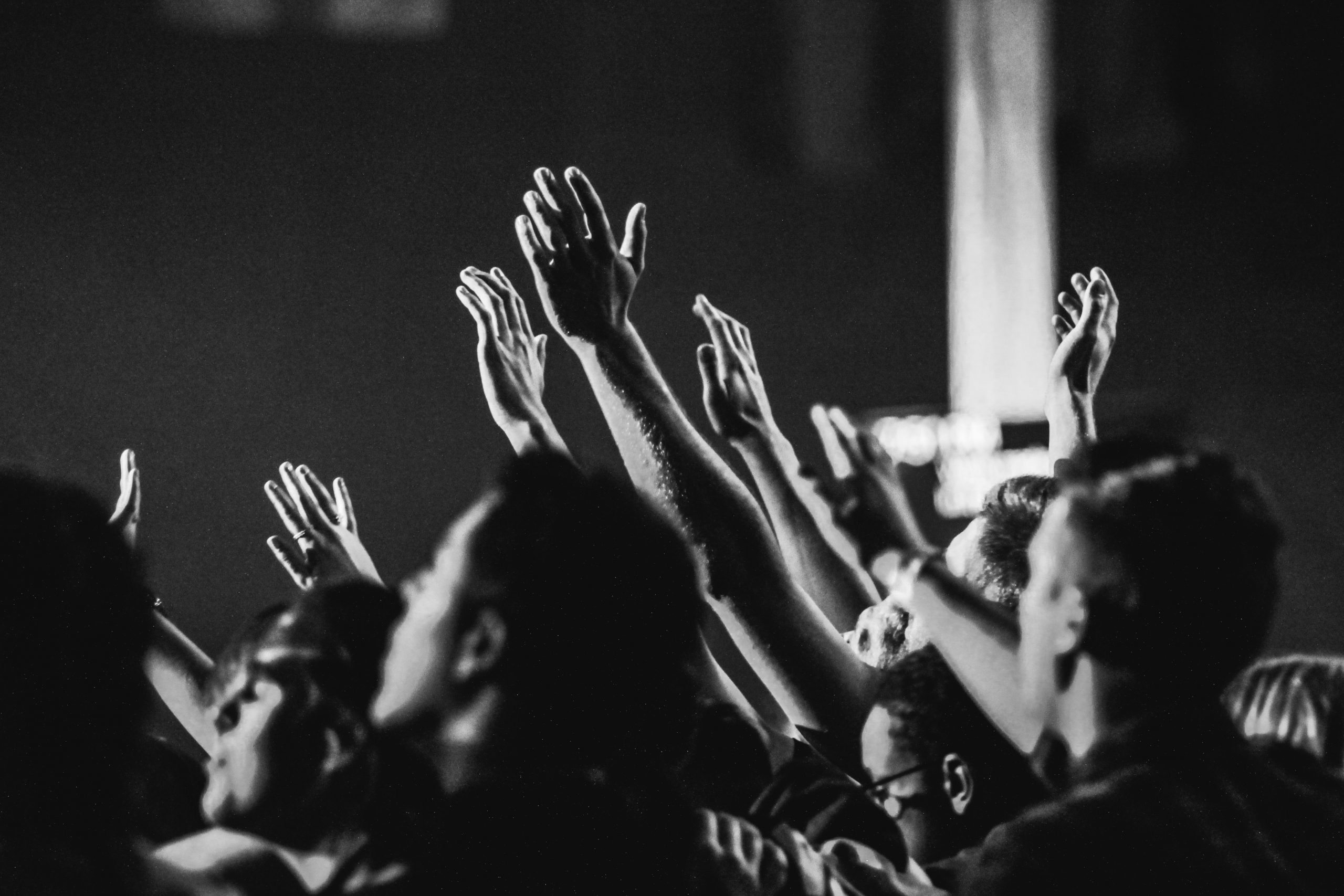 grayscale-photo-of-people-raising-their-hands-1666816